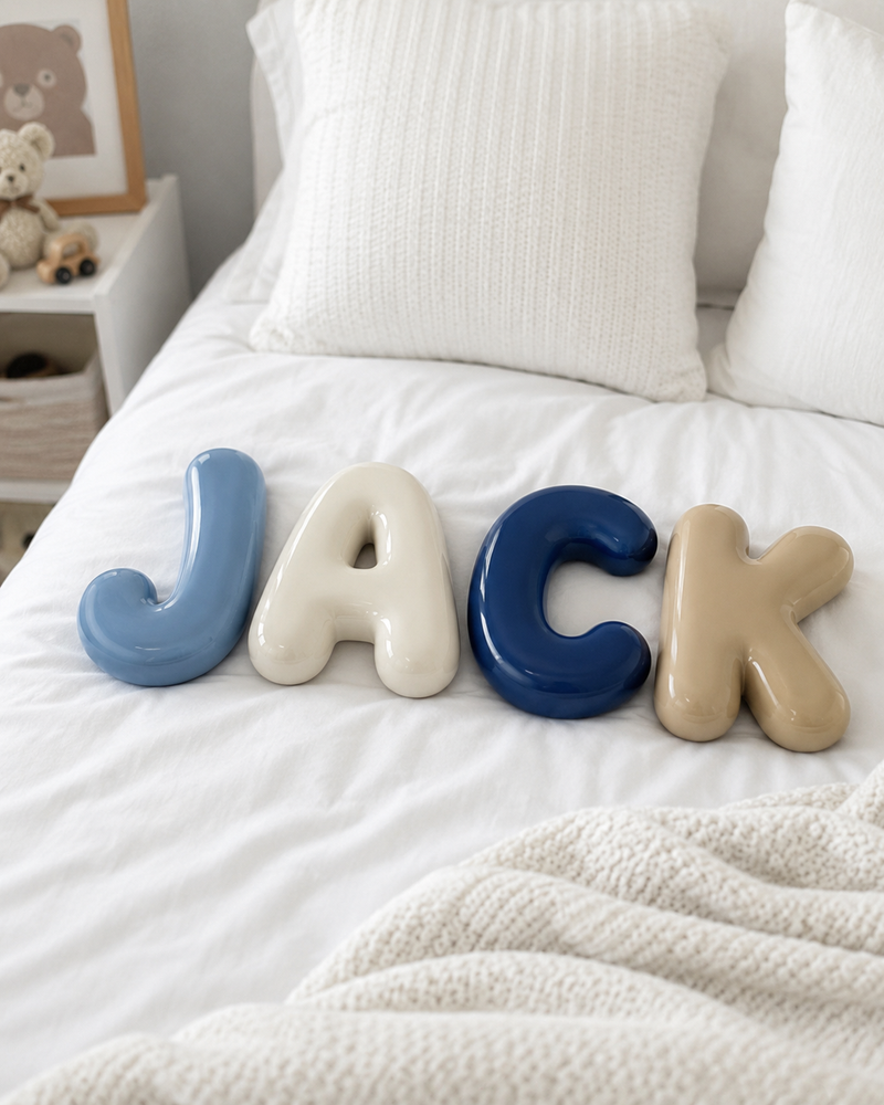 Glossy 3D printed bubble letters spelling JACK on a bed